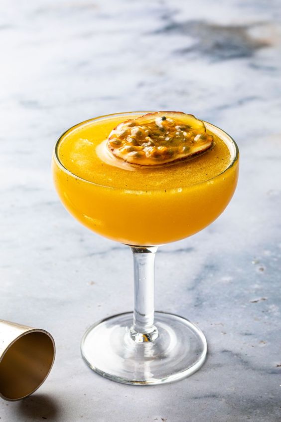 cocktail de aguardente medronho e maracujá. taça cocktail alta e decoração de meio maracuja, fundo marmore claro