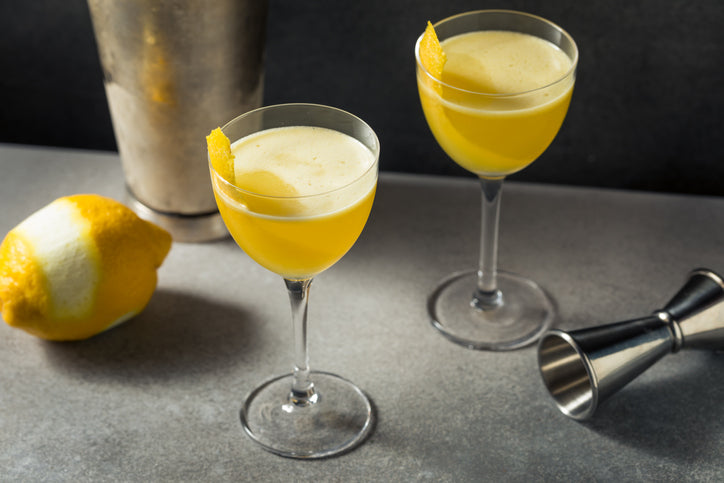 2 copos de cocktail com aguardente de medronho mel e limao num bar , com utensilios de barman
